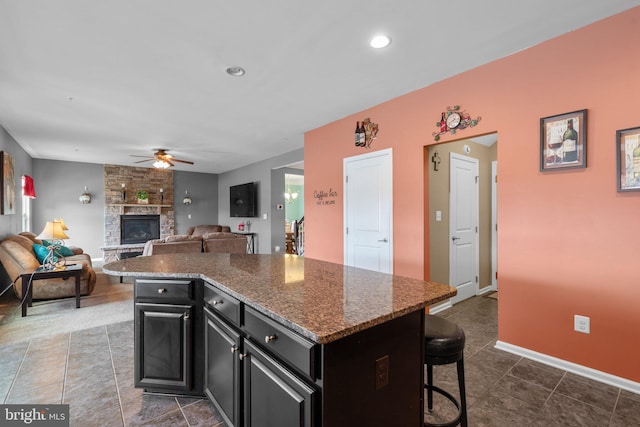 kitchen featuring a breakfast bar area, a fireplace, a ceiling fan, dark cabinets, and a kitchen island