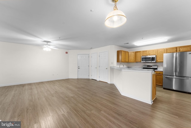 kitchen featuring a peninsula, a ceiling fan, stainless steel appliances, light countertops, and light wood-style floors
