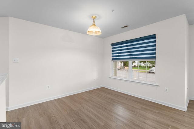 empty room featuring visible vents, wood finished floors, and baseboards