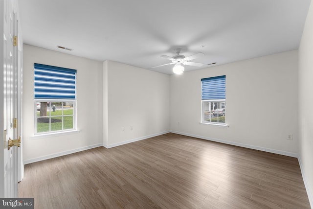 spare room with baseboards, a ceiling fan, visible vents, and wood finished floors