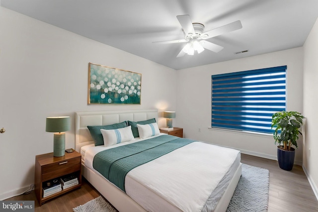 bedroom with baseboards, a ceiling fan, visible vents, and wood finished floors