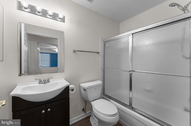 bathroom featuring toilet, baseboards, bath / shower combo with glass door, and vanity