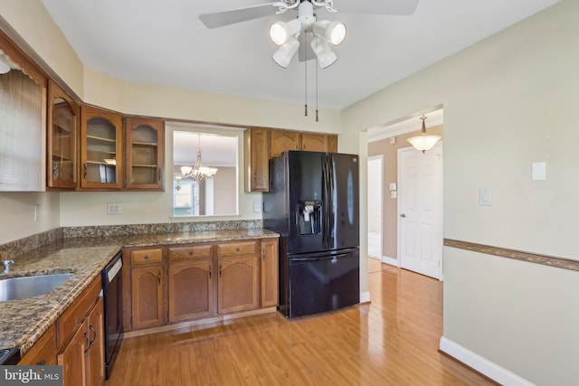 kitchen featuring glass insert cabinets, light wood-style floors, black appliances, brown cabinetry, and ceiling fan with notable chandelier