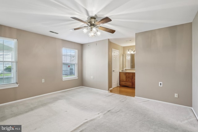 unfurnished bedroom featuring visible vents, ensuite bathroom, baseboards, light carpet, and a ceiling fan