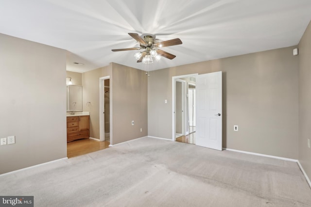 unfurnished bedroom featuring light colored carpet, connected bathroom, a ceiling fan, and baseboards