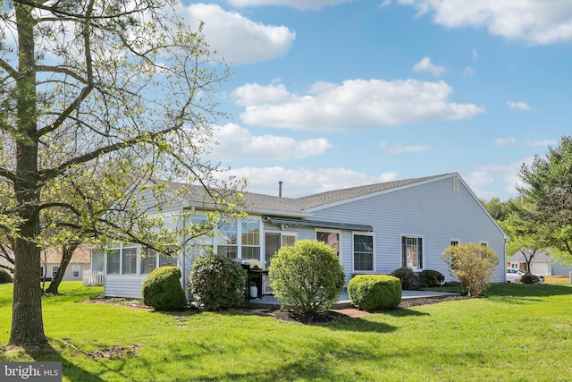 exterior space with roof with shingles, a yard, a patio, and a sunroom