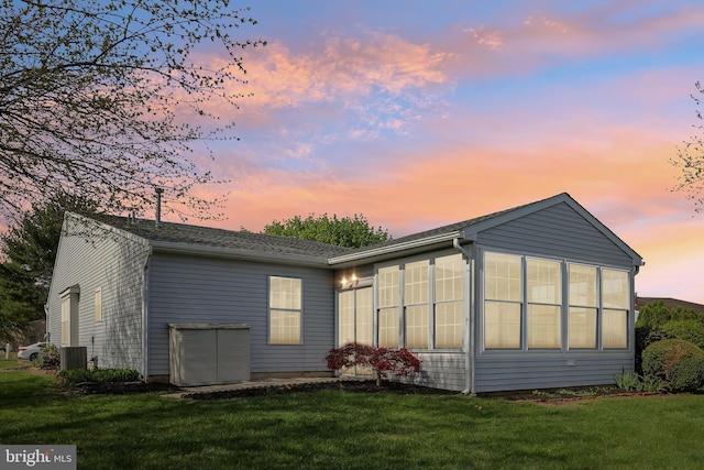 back of house at dusk with central AC unit, a yard, and a sunroom