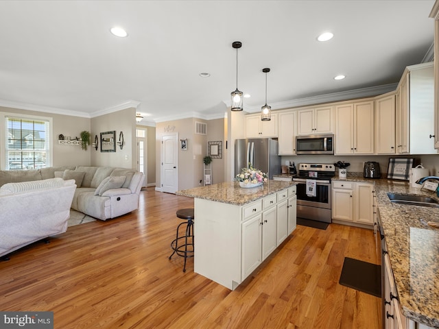 kitchen featuring a sink, light wood-style floors, ornamental molding, appliances with stainless steel finishes, and open floor plan