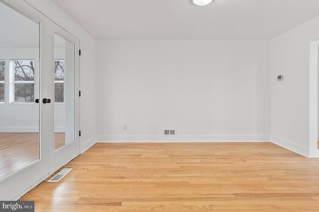 empty room featuring light wood finished floors, visible vents, french doors, and baseboards