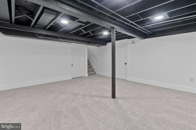 finished basement with baseboards, stairway, and light colored carpet