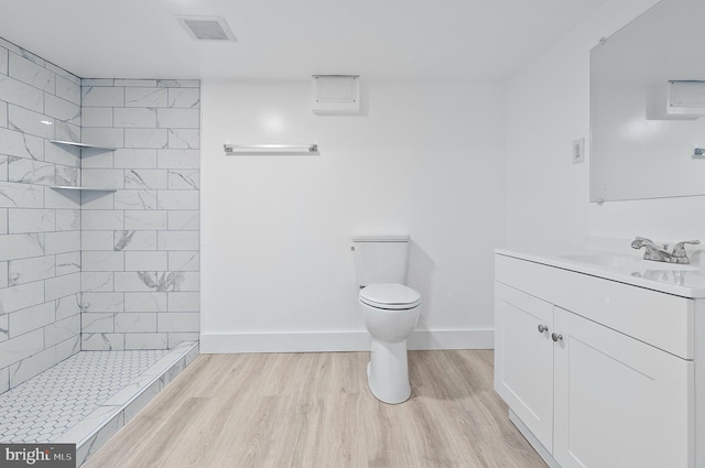 full bath with vanity, toilet, a tile shower, visible vents, and wood finished floors
