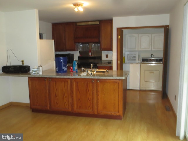 kitchen with washing machine and clothes dryer, a peninsula, a sink, and light wood finished floors