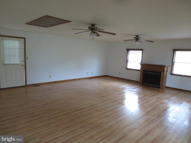 unfurnished living room with attic access, a fireplace, baseboards, and light wood-type flooring