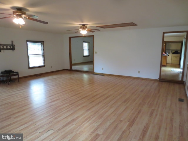 spare room featuring light wood finished floors, attic access, a ceiling fan, and baseboards