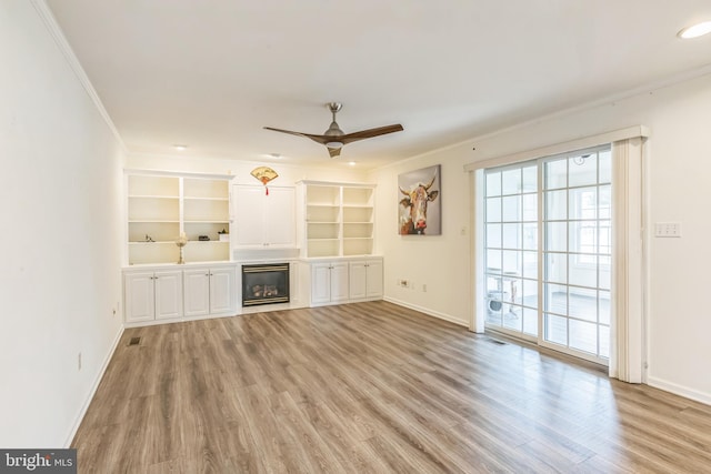 unfurnished living room with a ceiling fan, light wood-type flooring, crown molding, baseboards, and a glass covered fireplace