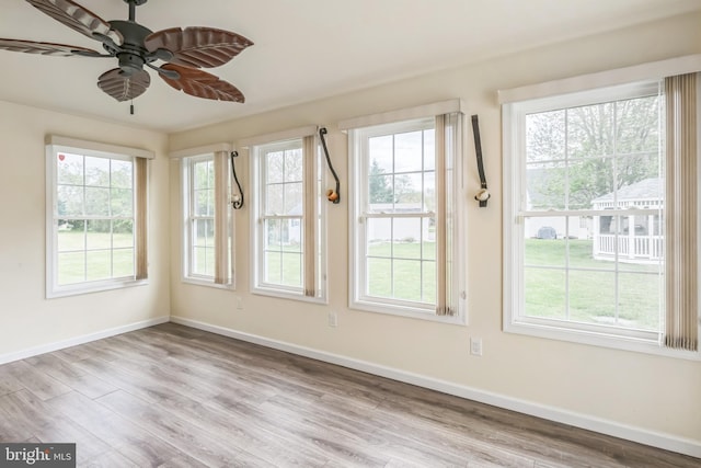 unfurnished sunroom with baseboards, wood finished floors, and a healthy amount of sunlight