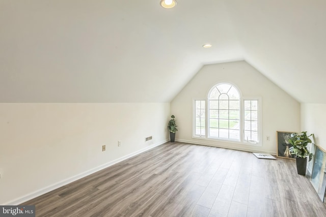 additional living space with vaulted ceiling, wood finished floors, visible vents, and baseboards