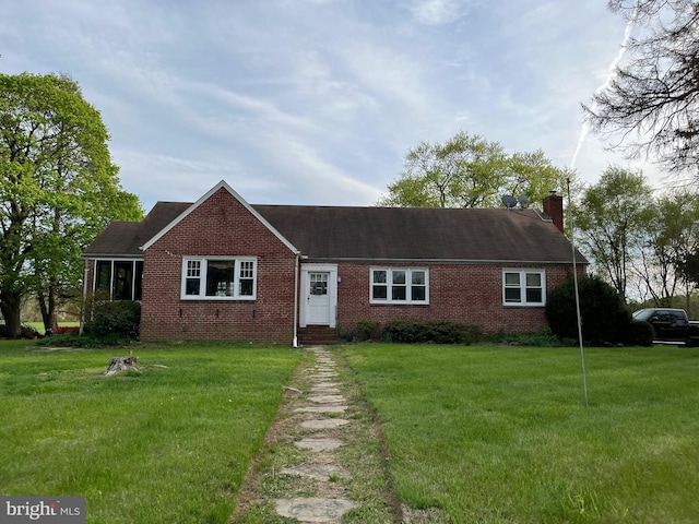 view of front of house featuring a shingled roof, a chimney, brick siding, and a front yard