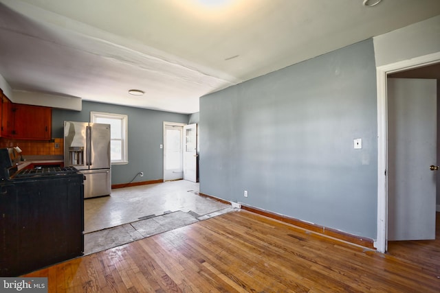 kitchen featuring baseboards, stainless steel refrigerator with ice dispenser, tasteful backsplash, light wood finished floors, and gas stove