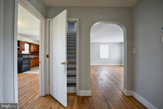 hallway featuring stairs, arched walkways, baseboards, and light wood-style floors