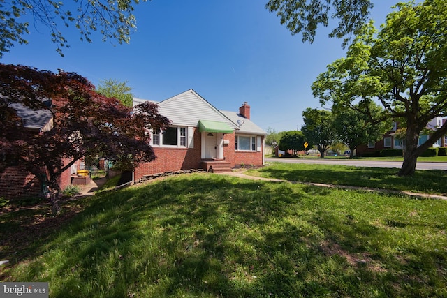 view of front of house with brick siding, a chimney, entry steps, and a front lawn