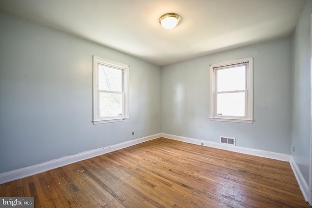 empty room featuring a healthy amount of sunlight, baseboards, hardwood / wood-style floors, and visible vents