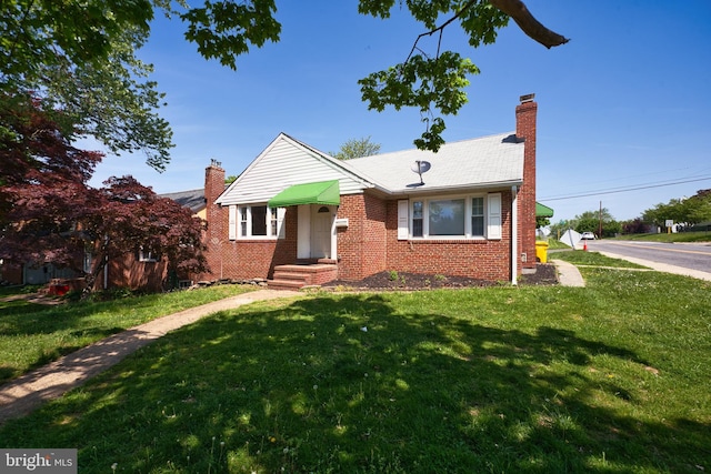 bungalow-style home with a chimney, brick siding, and a front yard