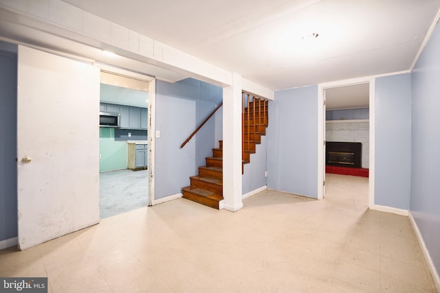 finished below grade area with baseboards, a brick fireplace, tile patterned floors, and stairway