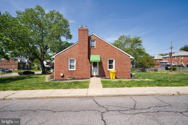 bungalow-style home featuring brick siding, a chimney, and a front yard