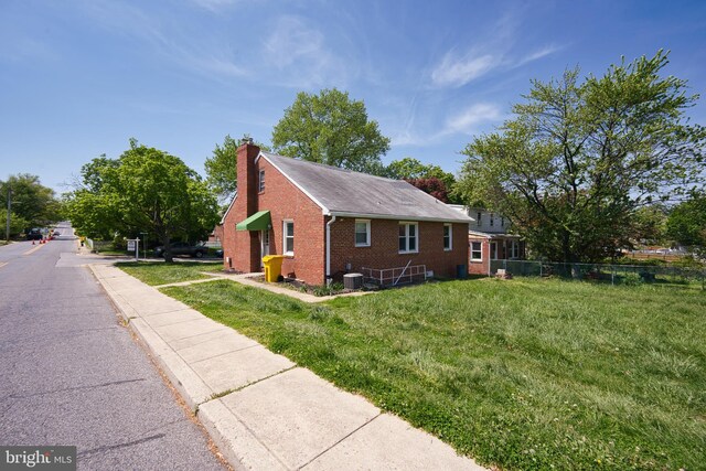 view of home's exterior featuring a chimney, brick siding, fence, cooling unit, and a yard
