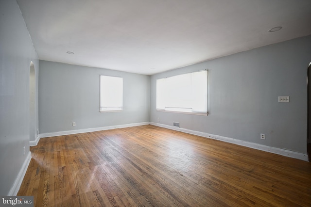 unfurnished room with arched walkways, baseboards, visible vents, and wood finished floors