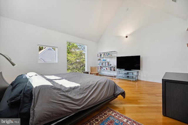 bedroom with high vaulted ceiling and wood finished floors