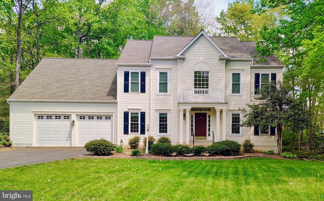 colonial inspired home with an attached garage, a front yard, roof with shingles, and driveway