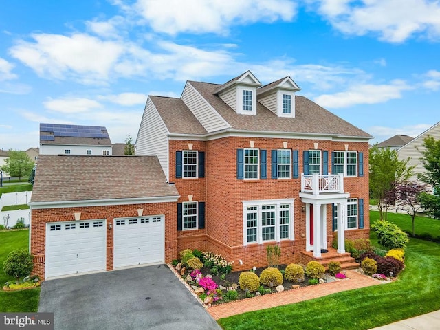 colonial-style house featuring brick siding, a garage, a balcony, driveway, and a front lawn