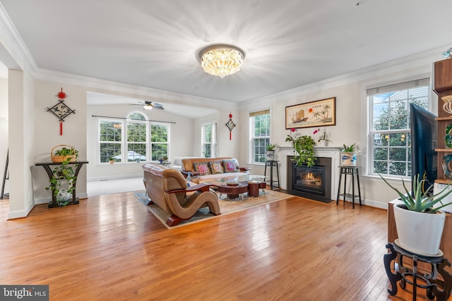 living room featuring light wood-type flooring, a fireplace with flush hearth, ornamental molding, a chandelier, and ceiling fan