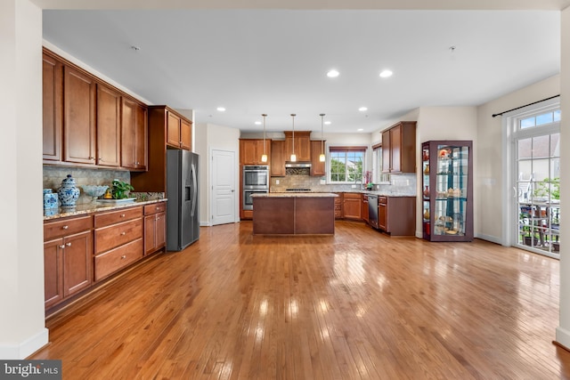 kitchen with appliances with stainless steel finishes, plenty of natural light, light wood finished floors, a kitchen island, and recessed lighting