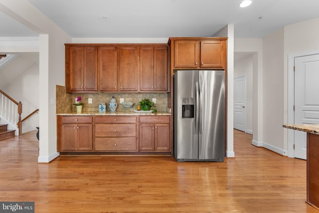 kitchen featuring stainless steel refrigerator with ice dispenser, tasteful backsplash, brown cabinetry, light wood-style flooring, and light stone counters