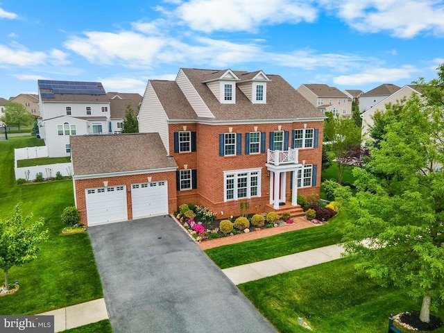 georgian-style home featuring brick siding, a garage, a balcony, asphalt driveway, and a residential view