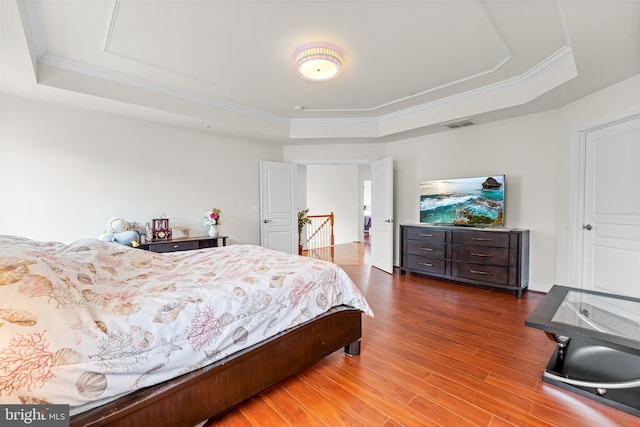bedroom with a raised ceiling, wood finished floors, and ornamental molding