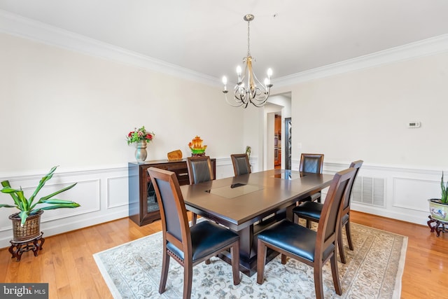 dining space with a chandelier, ornamental molding, a wainscoted wall, light wood-style floors, and a decorative wall