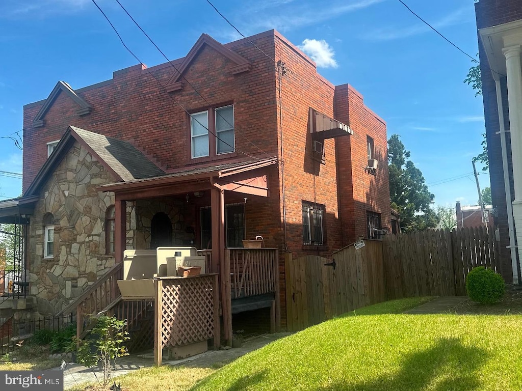 rear view of house with brick siding, a yard, stone siding, and fence