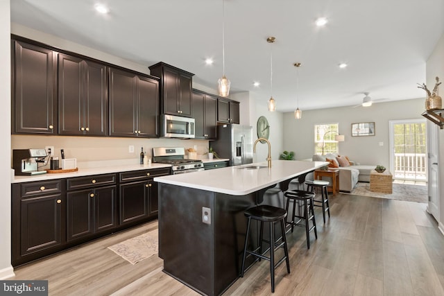 kitchen with a kitchen island with sink, a kitchen bar, appliances with stainless steel finishes, a sink, and open floor plan