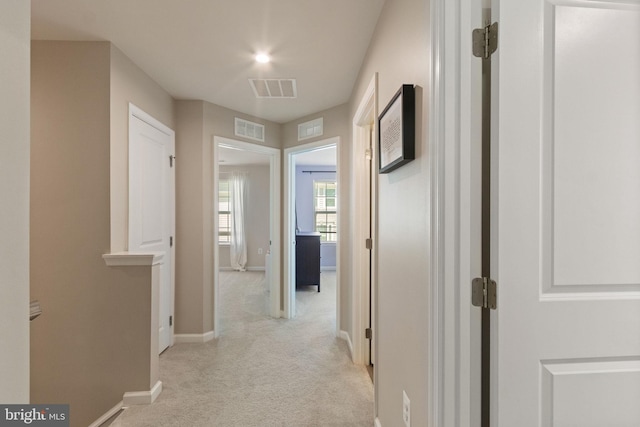 hallway featuring light colored carpet, baseboards, and visible vents