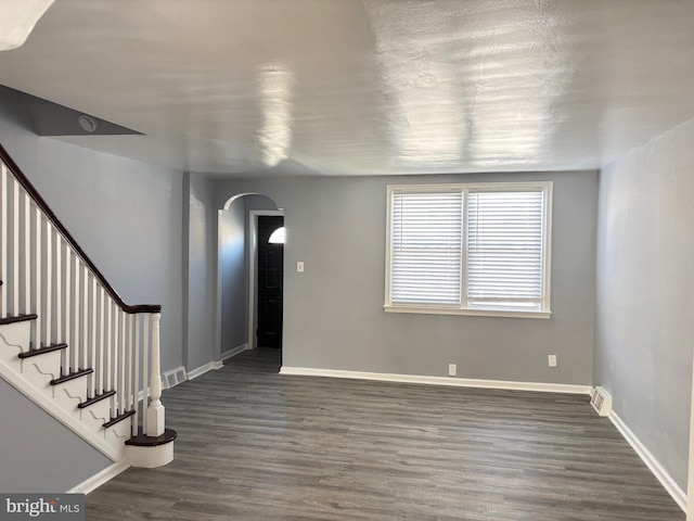 interior space with stairway, arched walkways, baseboards, dark wood-type flooring, and visible vents