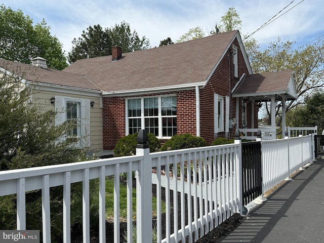 view of side of property with covered porch, a chimney, brick siding, fence, and a shingled roof
