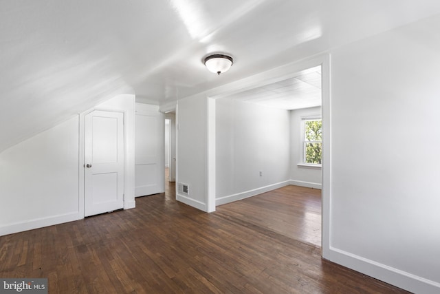 additional living space with dark wood-style flooring, baseboards, visible vents, and lofted ceiling