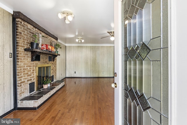 interior space with ornamental molding, wood finished floors, a fireplace, baseboards, and a ceiling fan