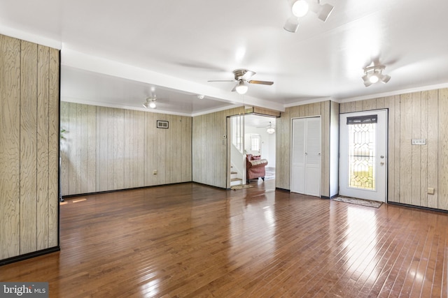 unfurnished living room with ceiling fan, crown molding, stairway, wooden walls, and hardwood / wood-style floors