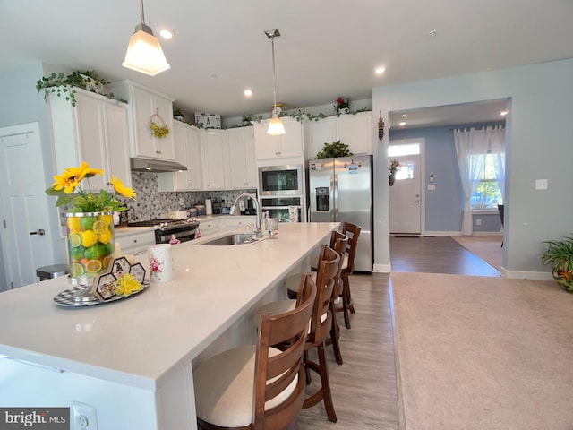 kitchen with white cabinets, stainless steel appliances, under cabinet range hood, and a sink
