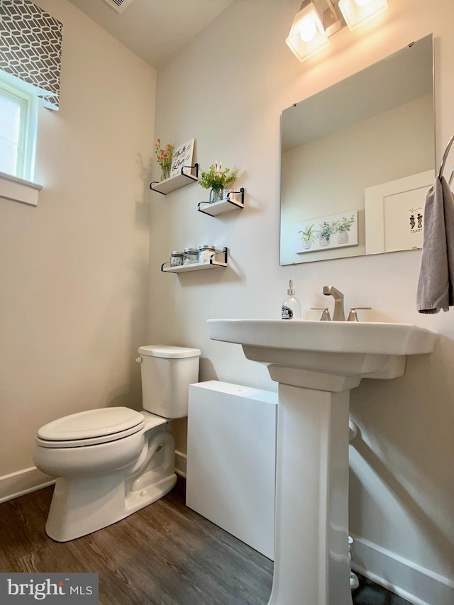 half bath with baseboards, wood finished floors, and toilet